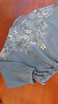 an old pair of jeans with floral embroidered on the front and back, sitting on a wooden surface