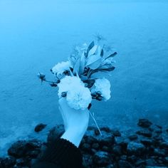 a person holding flowers in their hand near the water