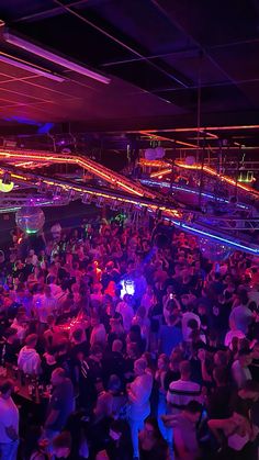 a large group of people standing around in a room with neon lights on the ceiling