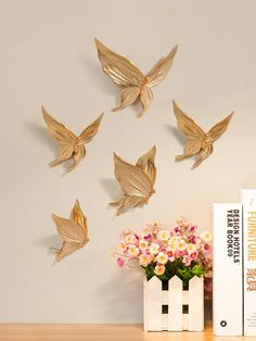 gold butterflies on the wall next to a book and vase with pink flowers in it