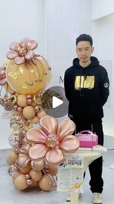 a man standing next to a tall balloon sculpture with flowers on it's side