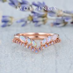 an image of a rose gold ring with opal stones on the side and flowers in the background