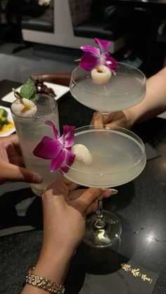 two people are holding glasses with drinks on the table and one is holding a flower