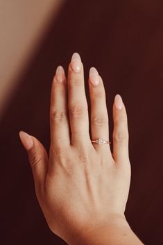 a woman's hand with a diamond ring on her left hand, against a brown background