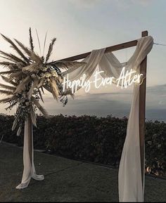 a wedding arch decorated with white flowers and greenery for an outdoor ceremony at sunset