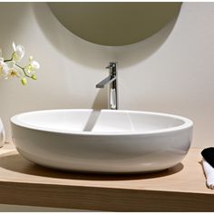 a white bowl sink sitting on top of a wooden counter next to a round mirror