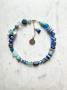 ABOUT THIS PIECE: "Santorini" necklace.  Handcrafted, one-of-a-kind, eco-friendly piece entailing: recycled glass, shells, tiny cotton tassels, Swarovski Crystal,  semi-precious stones, coin from Afghanistan pendant, handmade ceramic + paper beads, carved wood, seed bead and 14K gold vermeil hardware. 16" with a 2.5" extender.  Wear this statement necklace anywhere, be it a casual day with a white tee + jeans to a special occasion or on vacation.  I'm happy to custom make a necklace with the col Adjustable Blue Jewelry For Vacation, Unique Recycled Glass Necklaces For Beach, Unique Recycled Glass Beach Necklace, Handmade Ocean Color Necklaces For Beach, Beach Jewelry With Large Round Beads, Round Beach Jewelry With Large Beads, Ocean-inspired Blue Beaded Necklaces With Round Beads, Light Blue Round Bead Necklaces For The Beach, Light Blue Beaded Necklaces For The Beach