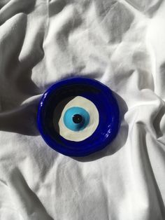 a blue and white bowl with an evil eye on the inside is laying on a white sheet