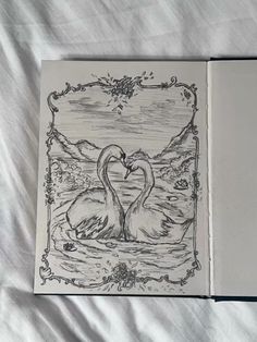 an open book with two swans in it on a white sheeted surface, the pages have been drawn