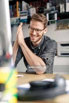 a man sitting at a desk with his hands together in front of him and smiling