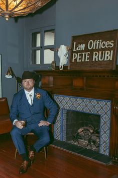 a man in a suit and hat sitting on a chair next to a fire place