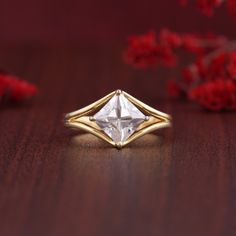 a close up of a ring on a wooden table with red flowers in the background