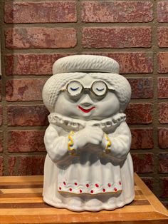 a white ceramic figurine sitting on top of a wooden table next to a brick wall