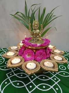 a small buddha statue sitting on top of a tray filled with pink flowers and lit candles