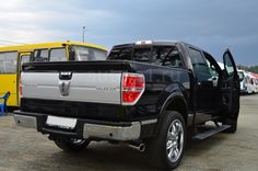 a black truck parked next to a yellow bus in a parking lot with other vehicles