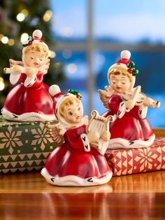 three christmas figurines sitting on top of a wooden table next to a tree