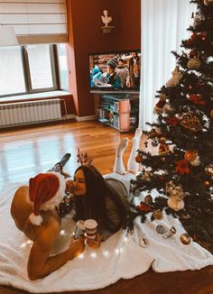 a woman in a santa hat sitting on the floor next to a christmas tree drinking beer