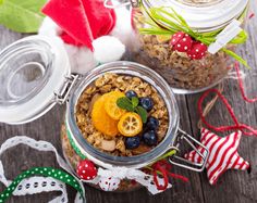 two glass jars filled with granola and fruit on top of a wooden table next to christmas decorations