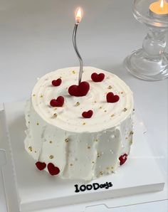 a white cake with red hearts on it and a single candle in the middle that says 100 days