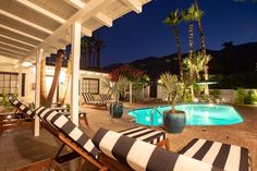 an outdoor pool with lounge chairs and palm trees in the back yard at night time