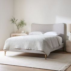 a bed with white sheets and pillows in a room next to a lamp on a dresser