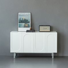 a white sideboard with two pictures on top and a radio next to it in front of a gray wall