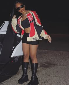 a woman standing next to a motorcycle in front of a white and black car at night