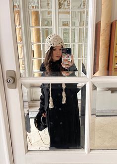 a woman taking a selfie in front of a mirror with her cell phone and hat on