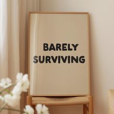 there is a framed sign that says barely surviving next to a vase with white flowers