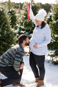 a man kneeling down to kiss a pregnant woman's belly in front of christmas trees