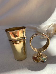 two gold colored cups sitting next to each other on a white cloth covered tablecloth