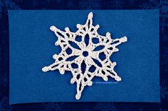 a crocheted snowflake is shown on a blue background with snow flakes