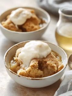 two small bowls filled with food next to a glass of wine and spoons on a table