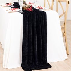 the table is set with white linens and red flowers on it, along with black velvet runneres