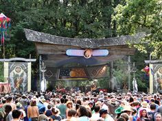 a large group of people standing in front of an outdoor stage with banners on it