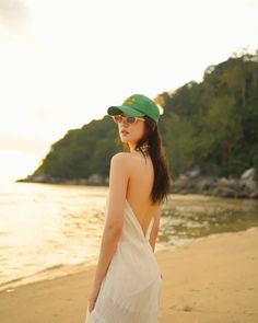 a woman standing on top of a beach next to the ocean wearing a green hat