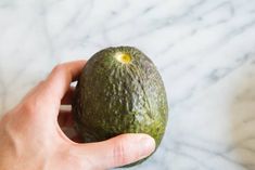 a person holding an avocado in their hand on a marble countertop top