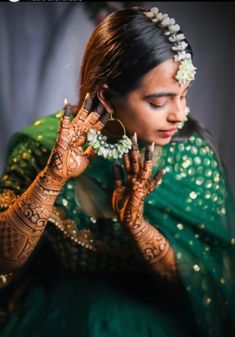 a woman in green and gold holding her hands up to her face with hendi