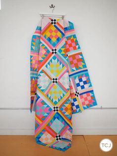 a multicolored quilt hanging on a wall next to a coat rack with clothes