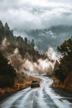 a car driving down a road in the middle of some trees and foggy mountains