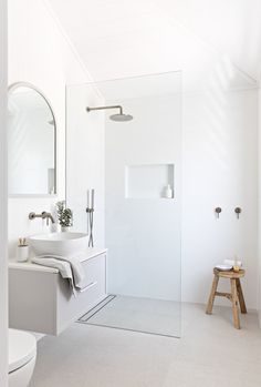 a white bathroom with a walk in shower next to a toilet and sink under a mirror