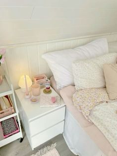 a white bed topped with lots of pillows next to a night stand filled with pink flowers