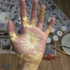 a person's hand with yellow paint on it and other art supplies in the background