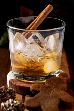 a glass filled with ice and cinnamon on top of a wooden table next to cookies