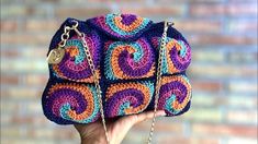 a hand holding a multicolored crocheted purse with chain attached to it