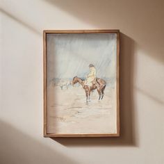 a painting hanging on the wall with a person sitting on a horse in the background