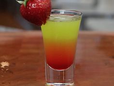 a strawberry on top of a drink in a tall glass with a green and red liquid