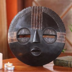 a wooden table topped with a black mask on top of it's face next to a candle