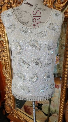 "This beautiful sequin tank is from the 50s by Harilea's Hong Kong. These are my favorite type of sweaters from the 50's. This one is especially elaborate. The wool base is covered with dense irridescent white sequins. There is an intricate pattern with tiny pearls and silver and white beading. Along the botton is border of 1.5\" pearl fringe. Fully lined in white silky fabric. Zips up the back with a metal zipper. It is labeled a size 36 and fits a size Medium, best, however, please see the mea Vintage Beaded Tops For Summer, Vintage Sleeveless Wedding Tops, White Beaded Top For Party, Vintage Embellished Tops For Summer, Vintage Beaded Fitted Tops, Vintage Fitted Beaded Tops, Fitted Vintage Beaded Tops, Festive Sleeveless Beaded Top, Festive Beaded Sleeveless Top