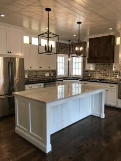 a large kitchen with an island in the middle of it and lots of lights hanging from the ceiling